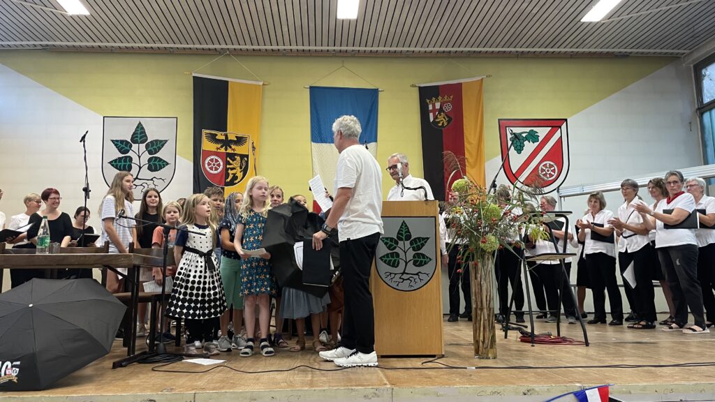 Links ein Kinderchor, rechts ein Chor von Erwachsenen auf einer Bühne