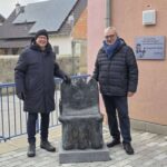 Zwei Männer vor einem Stuhl aus Bronze auf einem Sockel.