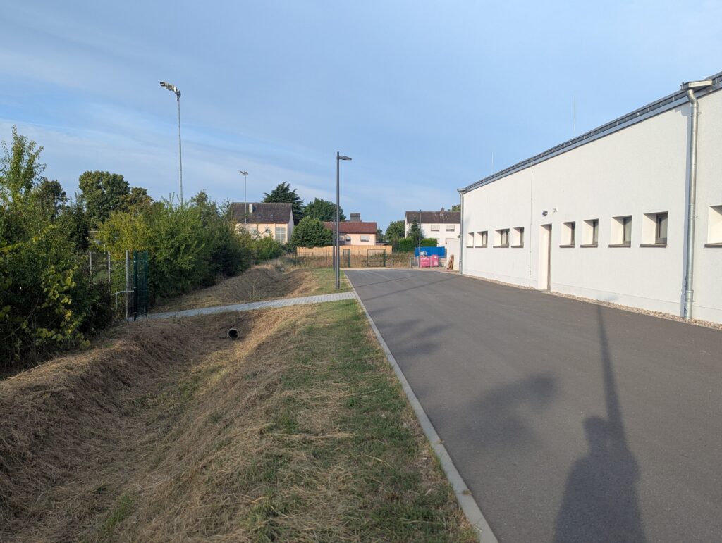 Links die Hecke zum Sportplatz, rechts der Umkleidetrakt mit dem Sportlereingang.